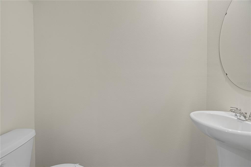 A half bathroom features a white pedestal sink, a round mirror, and a toilet — 3176 GOOSE ROAD, DAVENPORT, FL