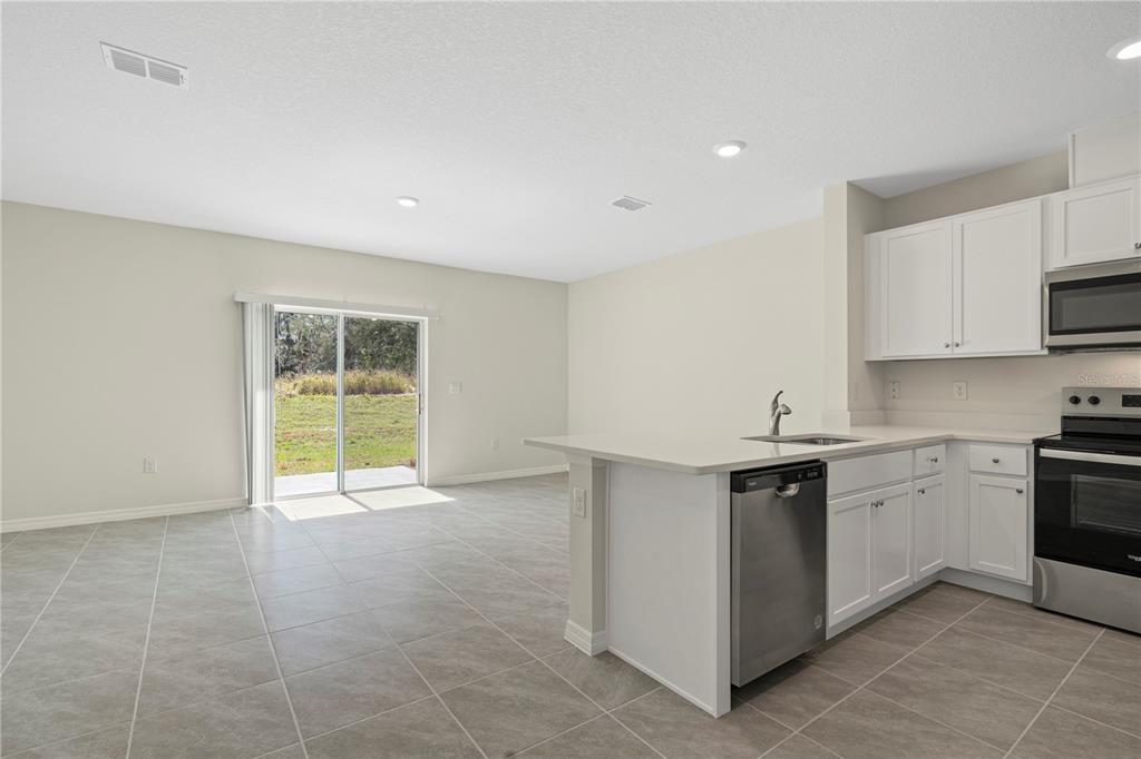 A kitchen with white cabinets and stainless steel appliances opens to a tiled living area — 3176 GOOSE ROAD, DAVENPORT, FL