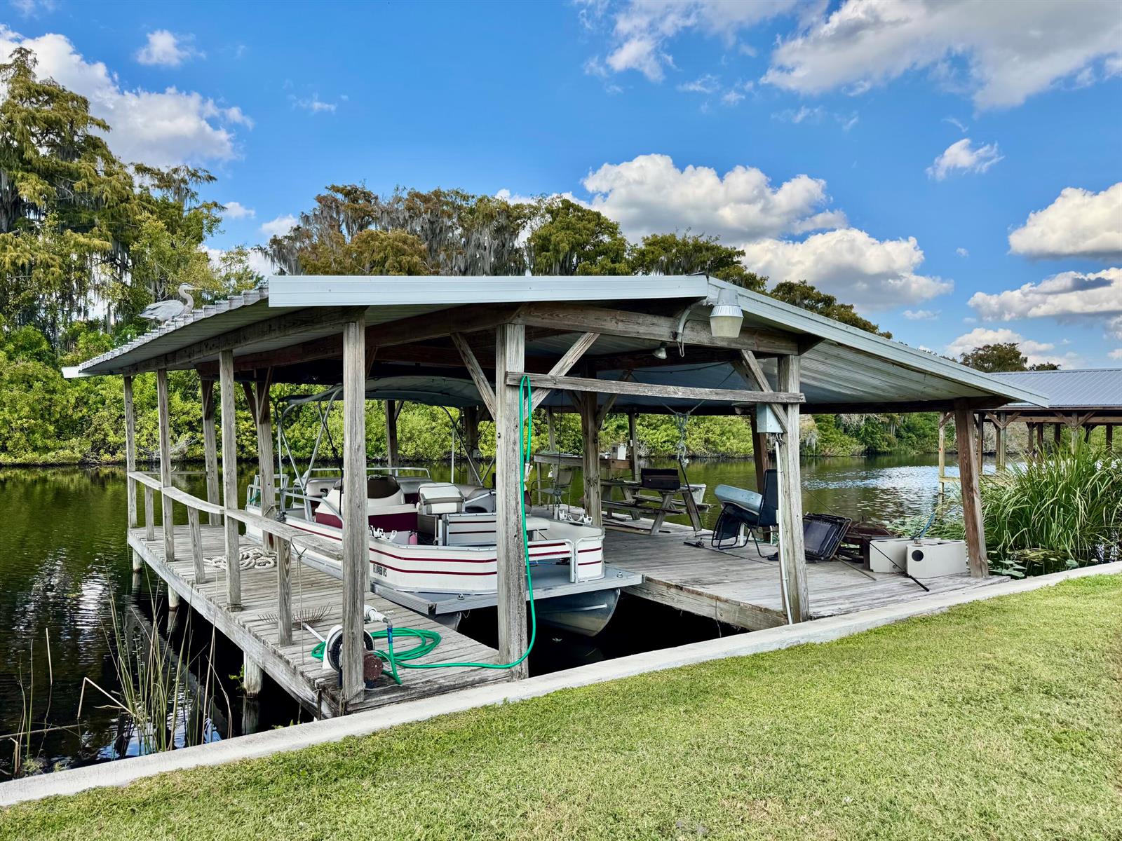 A covered wooden boat dock sits on a calm canal with a pontoon boat moored inside — 2091 SE 24th Boulevard, Okeechobee FL 34974, OKEECHOBEE, FL