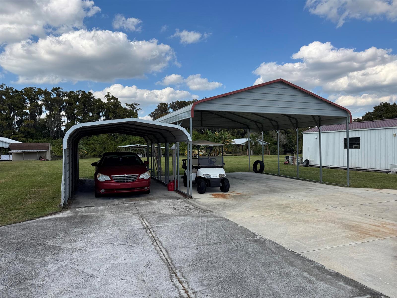 A red car and a golf cart are parked under two adjacent metal carports — 2091 SE 24th Boulevard, Okeechobee FL 34974, OKEECHOBEE, FL