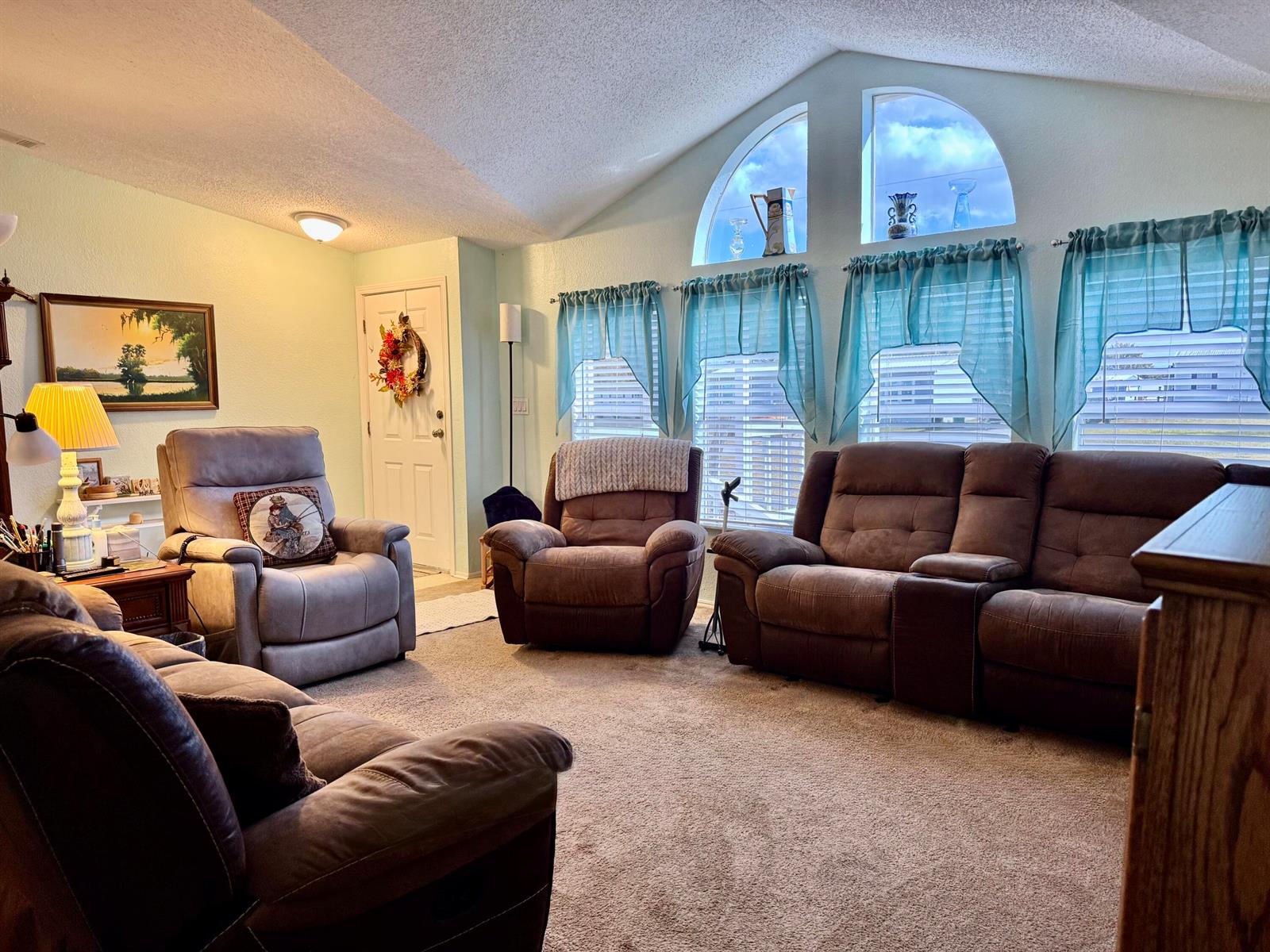 A living room features vaulted ceilings, arched windows, carpeted floors, and several brown reclining chairs — 2091 SE 24th Boulevard, Okeechobee FL 34974, OKEECHOBEE, FL