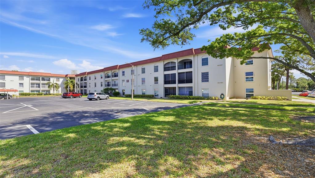 A multi-story apartment building with a parking lot and lawn in the foreground — 2700 BAYSHORE BOULEVARD UNIT 1307, DUNEDIN, FL