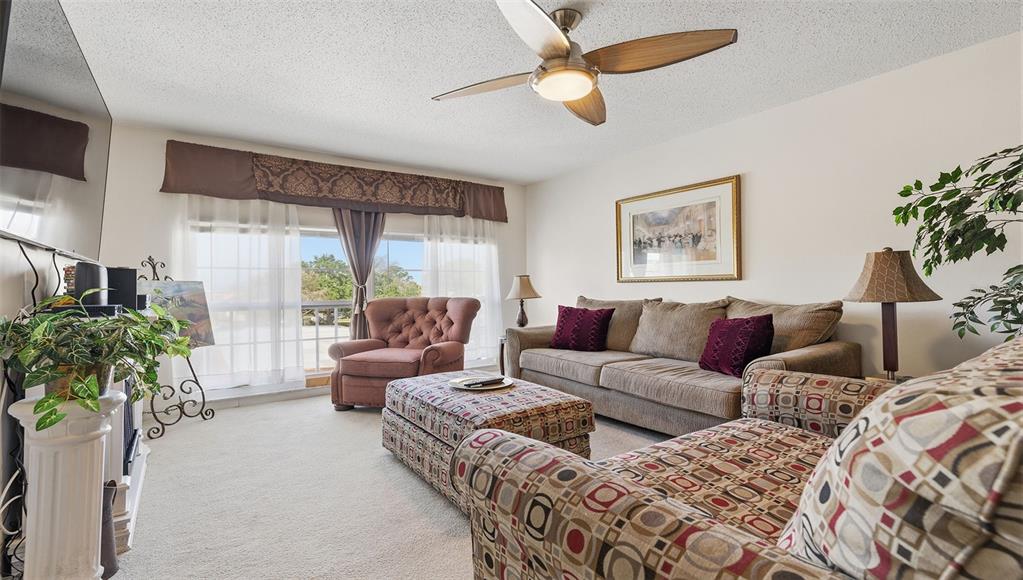 A living room features a ceiling fan, a sofa, patterned armchairs, and a large window — 2700 BAYSHORE BOULEVARD UNIT 1307, DUNEDIN, FL