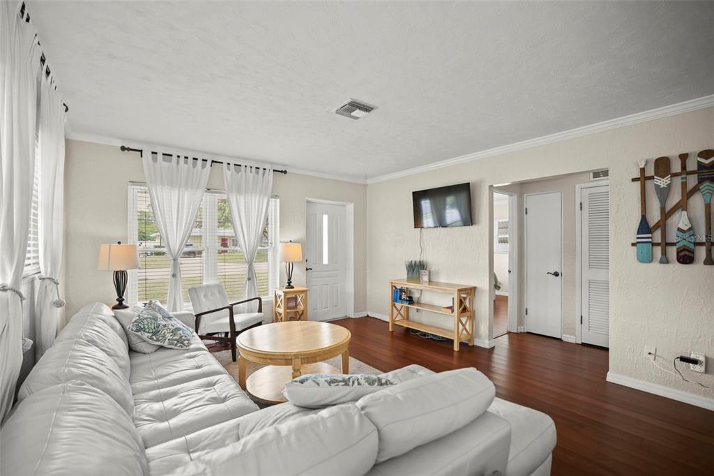 A living room features a white sectional sofa, wood flooring, and a wall-mounted television — 1121 SUNNYDALE DRIVE, CLEARWATER, FL