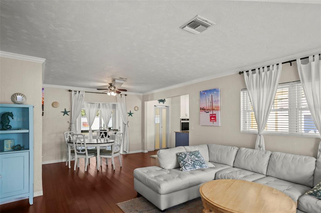 A living room with a white sectional sofa, wood flooring, and an adjacent dining area — 1121 SUNNYDALE DRIVE, CLEARWATER, FL