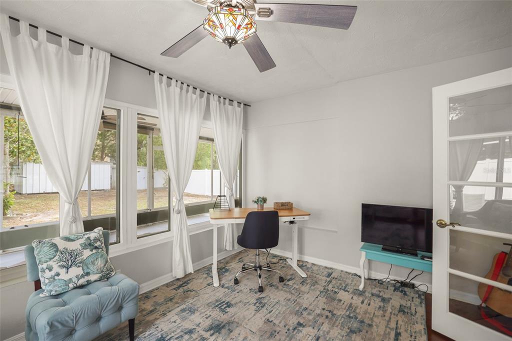 A home office features a desk, a blue armchair, a ceiling fan, and large windows — 1121 SUNNYDALE DRIVE, CLEARWATER, FL