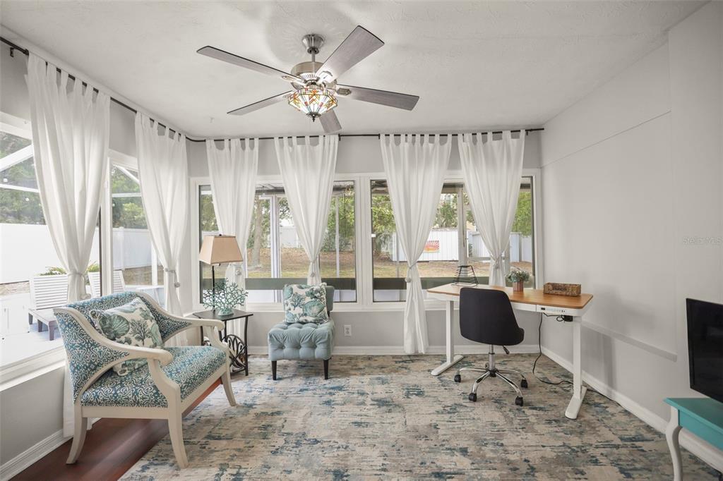 A sunroom features a ceiling fan, a desk, an armchair, and large windows with curtains — 1121 SUNNYDALE DRIVE, CLEARWATER, FL