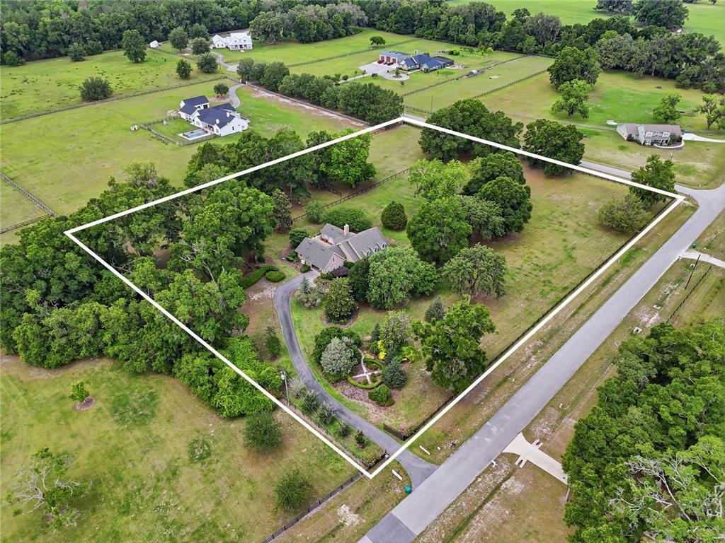 A tan house with a gray roof and three dormer windows sits behind a landscaped yard — 26341 NW 166TH AVENUE, HIGH SPRINGS, FL