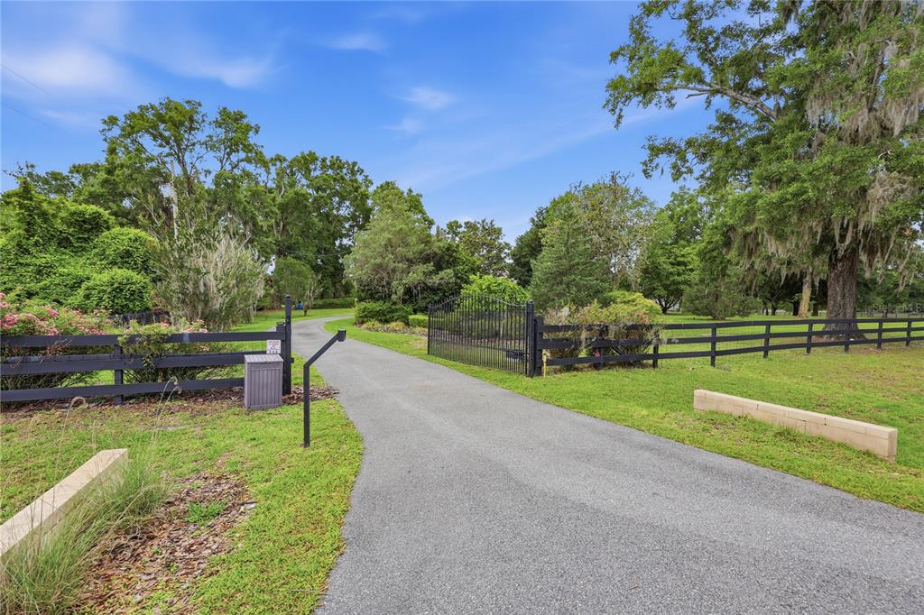 A paved driveway leads through an open black metal gate and wooden fence onto property — 26341 NW 166TH AVENUE, HIGH SPRINGS, FL