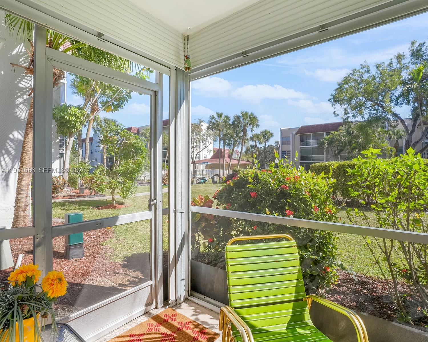A screened-in patio features a green chair, potted flowers, and a view of landscaping — 3531 Inverrary Dr # 107, Lauderhill FL 33319, LAUDERHILL, FL