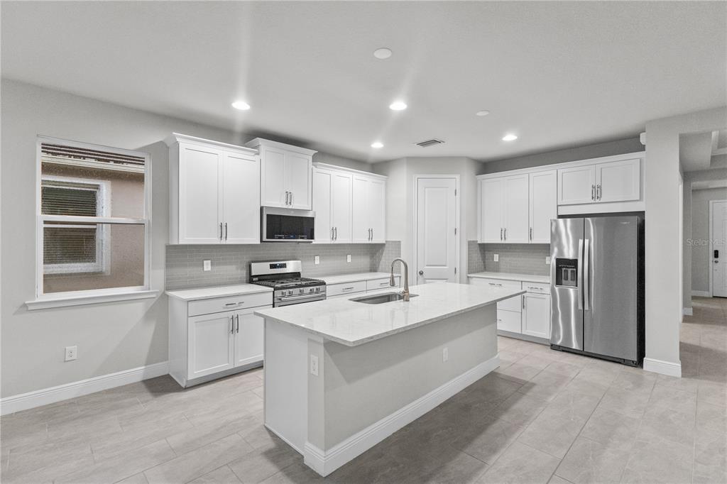 A modern kitchen features white cabinets, stainless steel appliances, a center island, and tile flooring — 8712 BAY MEADOW DRIVE, SARASOTA, FL