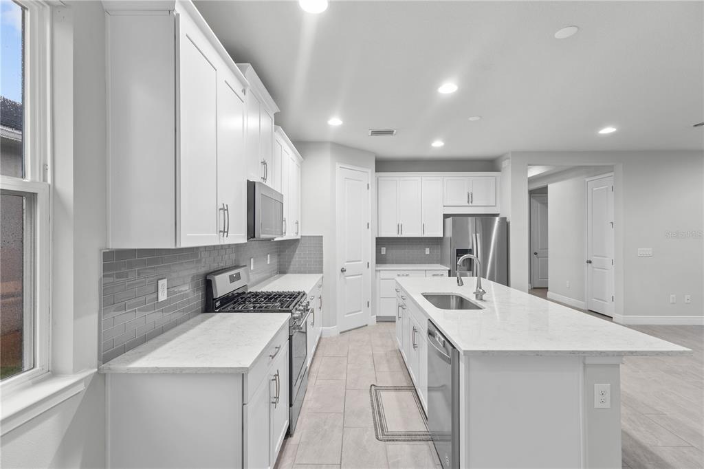 A modern kitchen features white cabinetry, a large quartz island, and gray subway tile backsplash — 8712 BAY MEADOW DRIVE, SARASOTA, FL