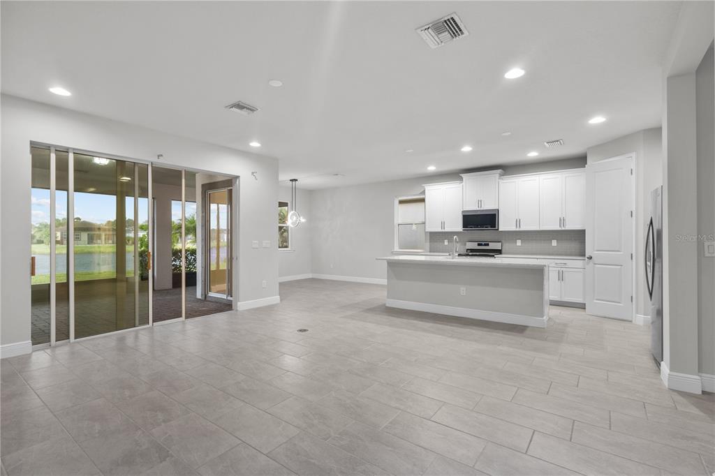 An open-concept kitchen and living area features white cabinetry, a central island, and sliding doors — 8712 BAY MEADOW DRIVE, SARASOTA, FL