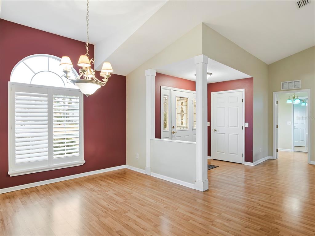 A dining room with hardwood floors, a chandelier, and a partial wall near the entryway — 1870 NW 56TH TERRACE, OCALA, FL