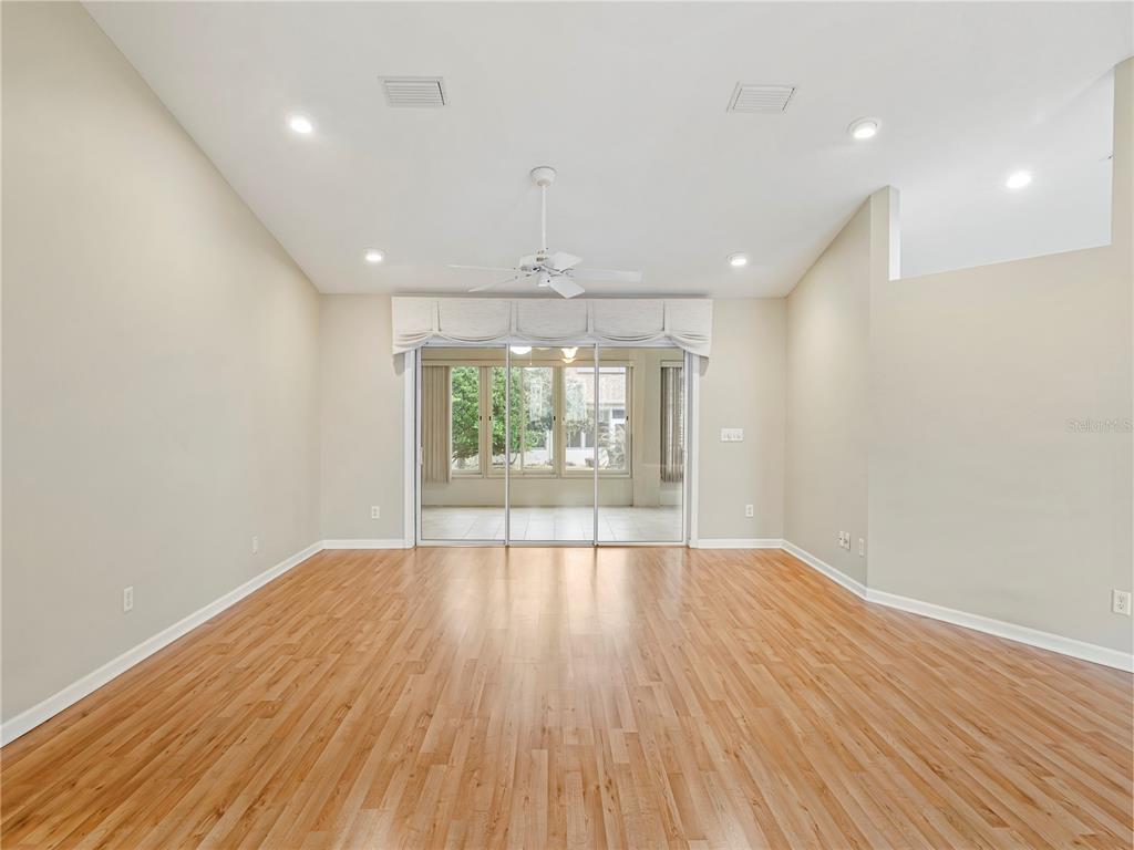 A spacious living room with light wood flooring, a vaulted ceiling, and sliding glass doors — 1870 NW 56TH TERRACE, OCALA, FL