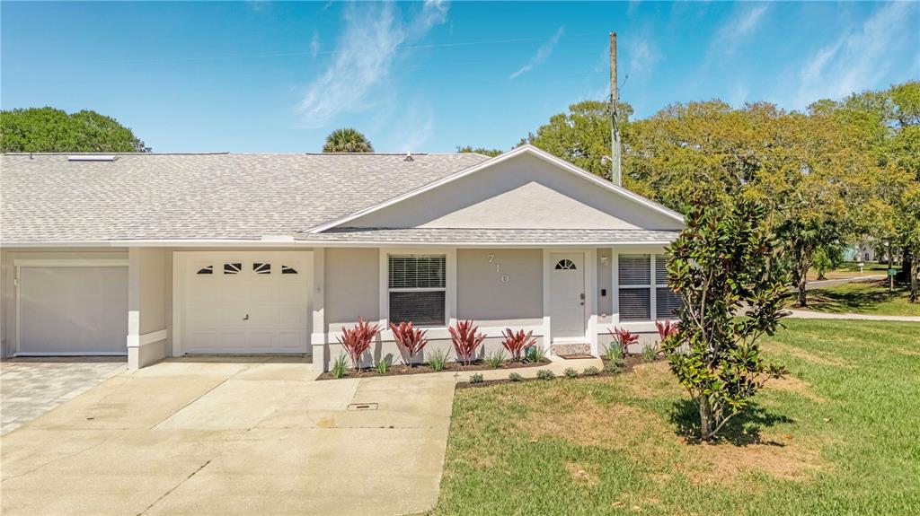 A single-story house exterior features a gray facade, a white garage door, and a driveway — 710 RIVER OAKS CIRCLE, NEW SMYRNA BEACH, FL