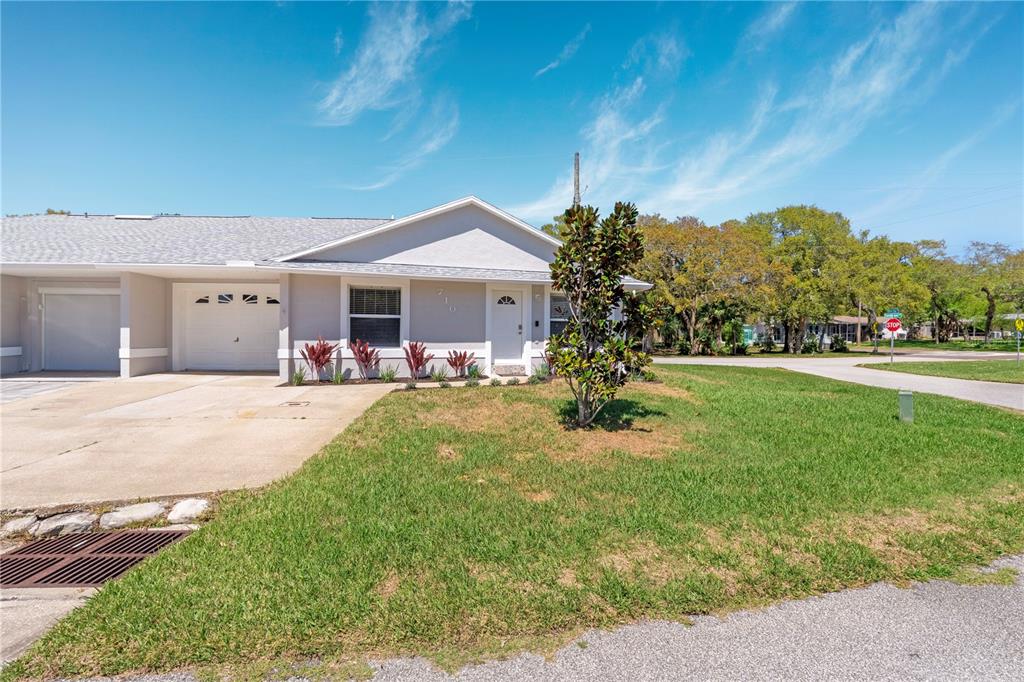 A single-story duplex with a white garage, a front door, and a small tree — 710 RIVER OAKS CIRCLE, NEW SMYRNA BEACH, FL