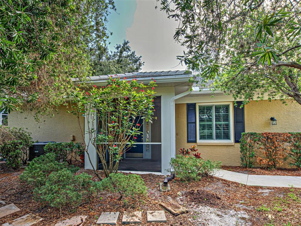 A tan house exterior features a screened-in front entryway, a window with shutters, and landscaping — 912 BARCLAY COURT, VENICE, FL