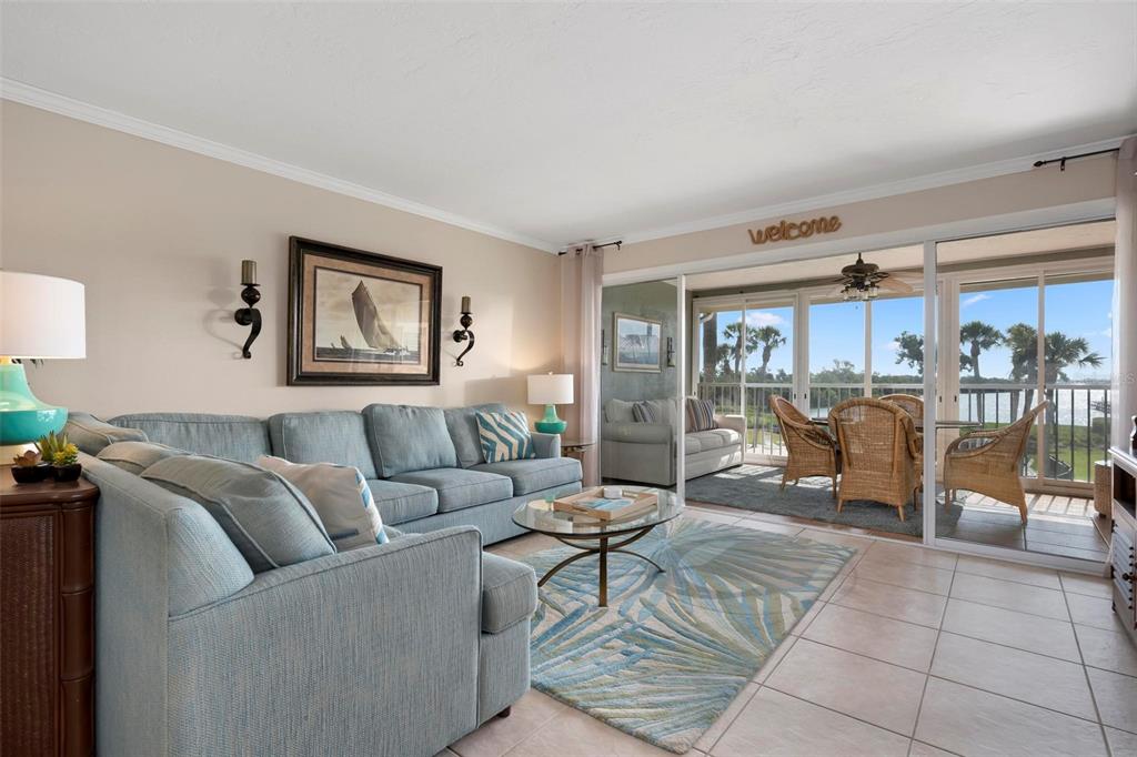 A living room with a blue sectional sofa, glass coffee table, and sliding doors to a balcony — 711 MANATEE AVENUE, HOLMES BEACH, FL
