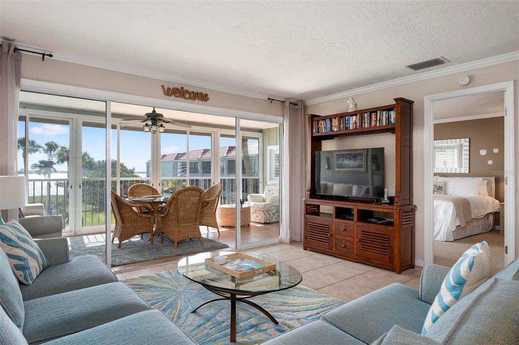 A living room with blue sofas, a glass coffee table, and a view of a balcony — 711 MANATEE AVENUE, HOLMES BEACH, FL