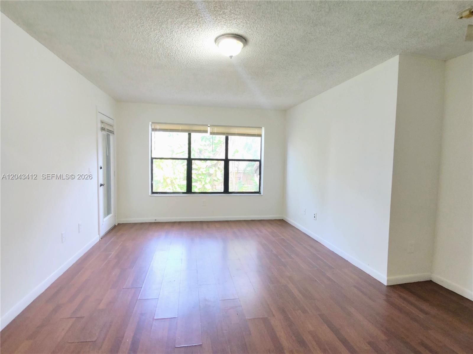 An empty room features white walls, wood-look flooring, a ceiling light, and a large window — 4241 W Mcnab Rd # 27, Pompano Beach FL 33069, POMPANO BEACH, FL
