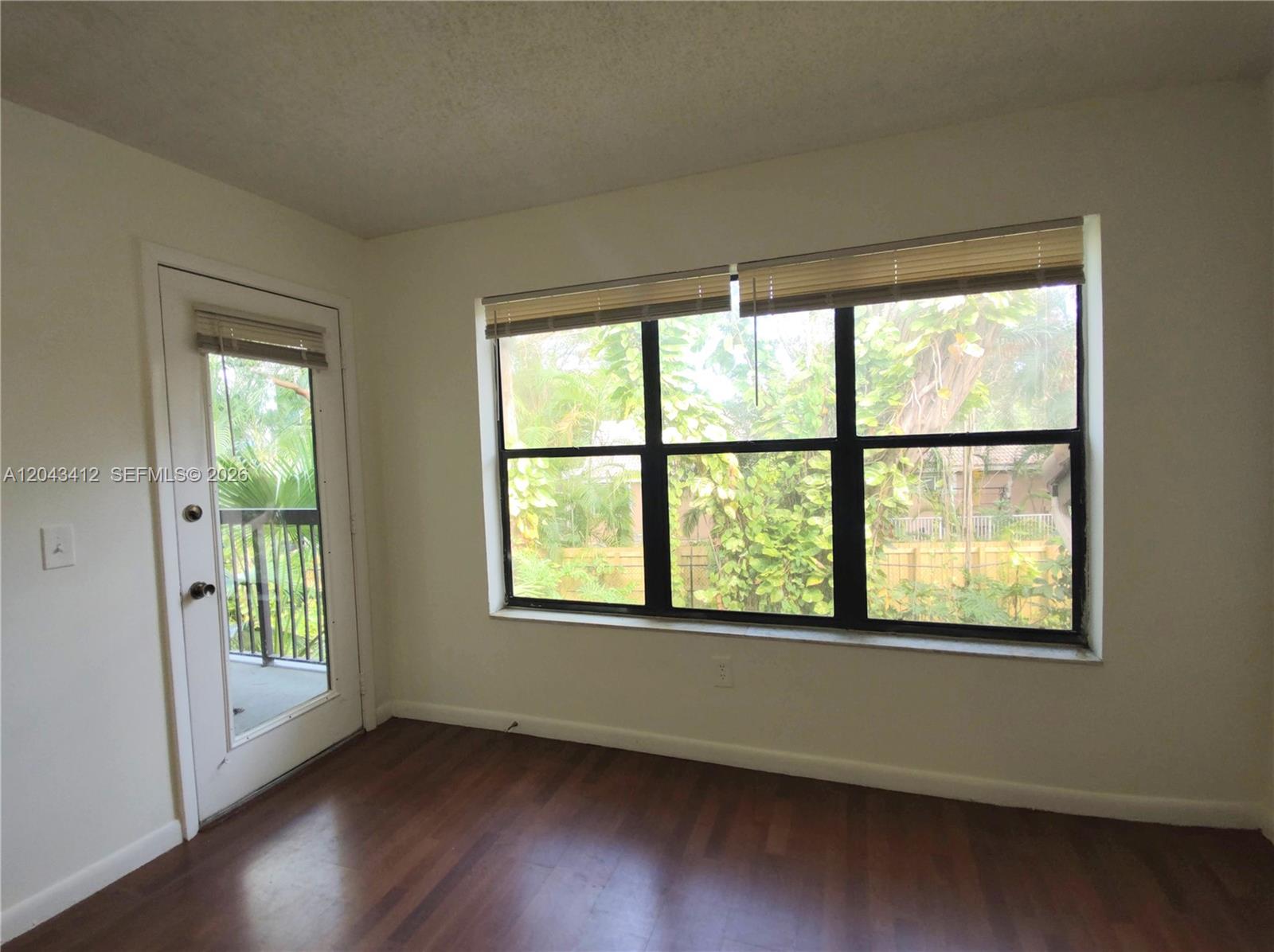 An empty room features dark wood flooring, a large window, and a glass-paneled door — 4241 W Mcnab Rd # 27, Pompano Beach FL 33069, POMPANO BEACH, FL