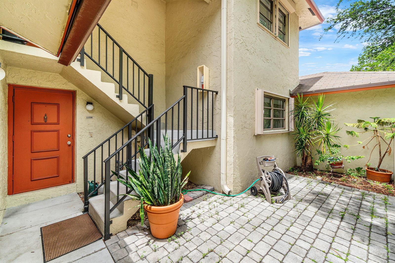 An exterior view shows a paved patio, a staircase with black railings, and an orange door — 1779 NE 39th Court # 1106, Pompano Beach FL 33064, POMPANO BEACH, FL