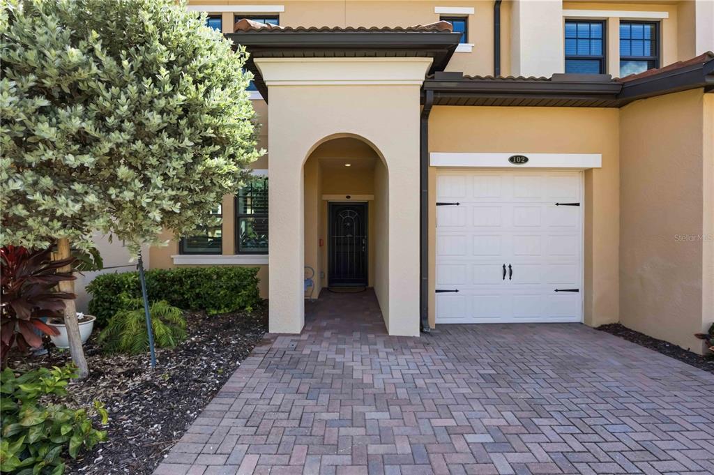 The exterior of a tan townhome features a paved driveway, a garage, and a covered entryway — 10055 CROOKED CREEK DRIVE UNIT 102, VENICE, FL