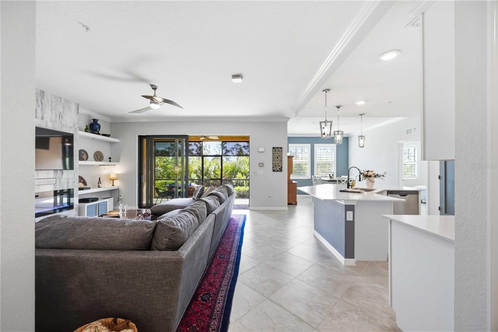 An open-concept living room and kitchen featuring tile floors, a gray sectional, and sliding doors — 10055 CROOKED CREEK DRIVE UNIT 102, VENICE, FL