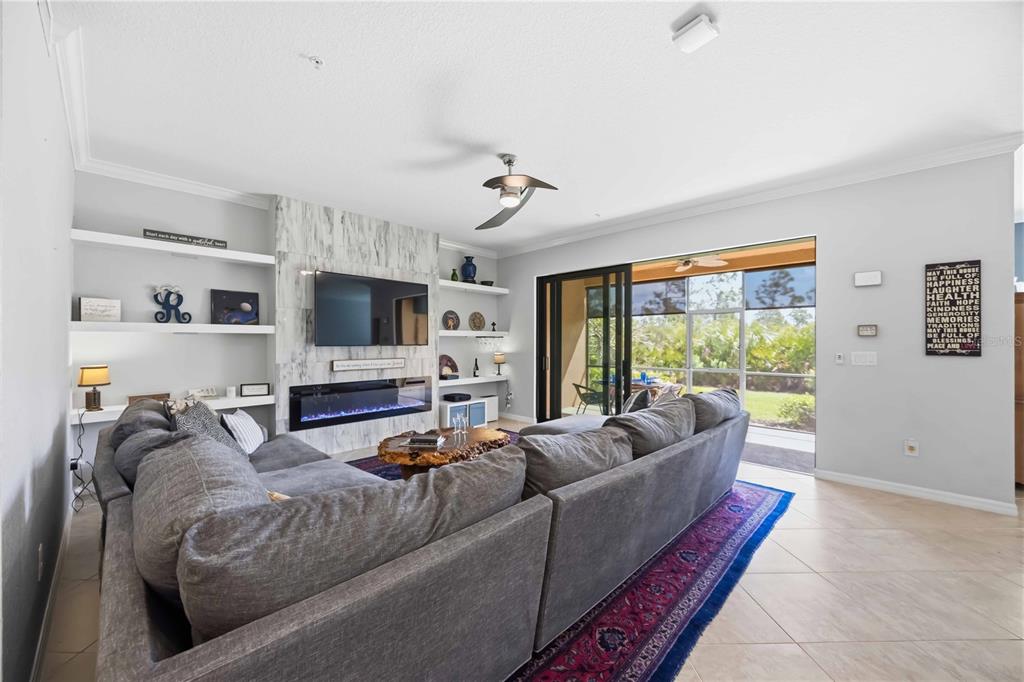 A living room features a gray sectional sofa, a marble fireplace with a TV, and sliding doors — 10055 CROOKED CREEK DRIVE UNIT 102, VENICE, FL