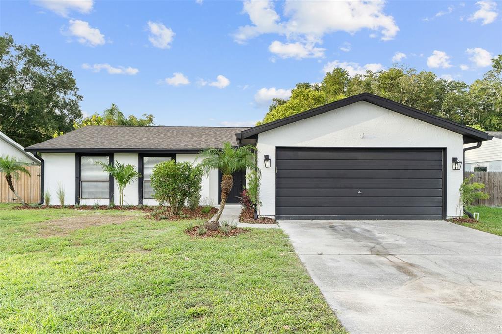 A single-story house with white stucco walls, a black garage door, and a dark roof — 5308 BLACK PINE DRIVE, TAMPA, FL