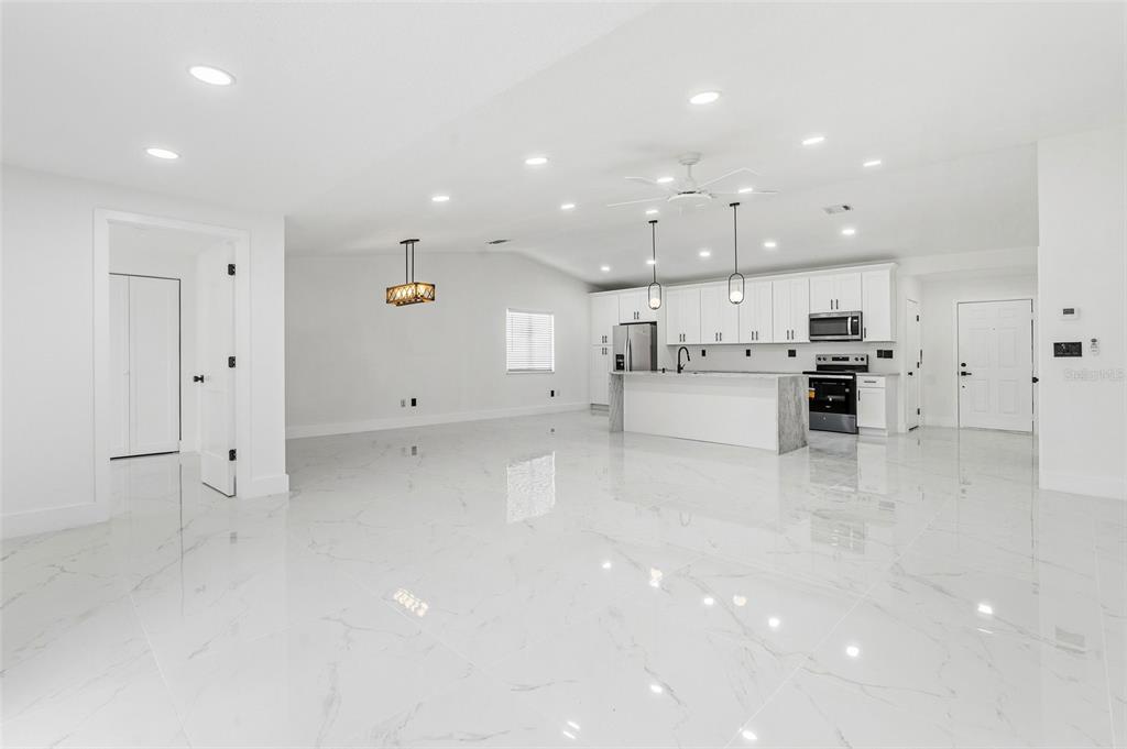 A bright, open-concept kitchen and living area features white cabinetry, marble-look tile flooring, and recessed lighting — 5308 BLACK PINE DRIVE, TAMPA, FL