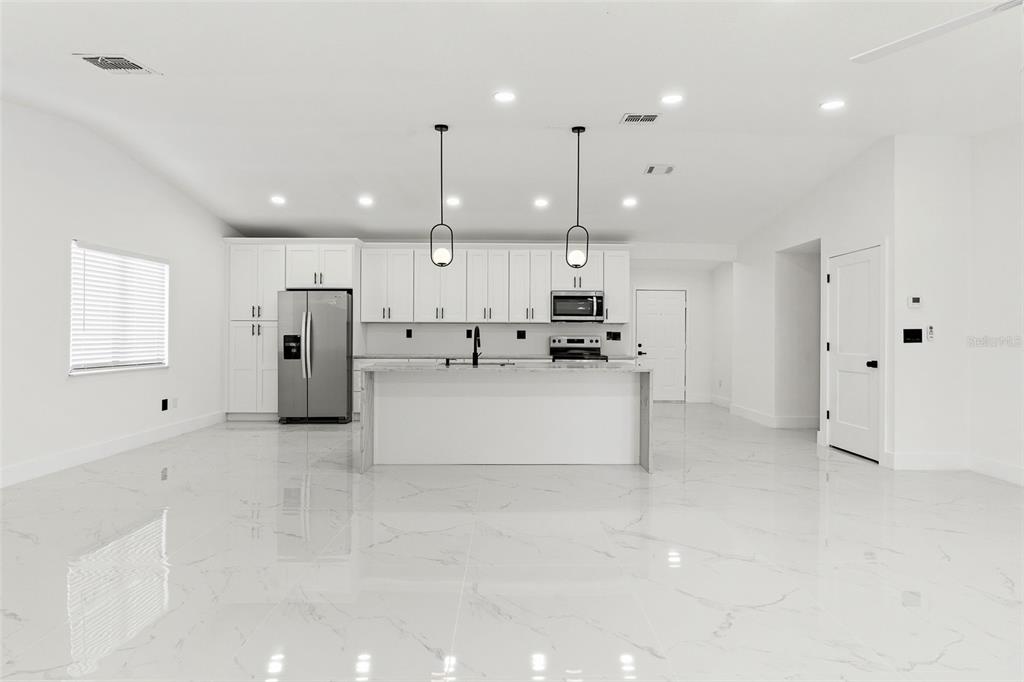 A modern kitchen features white cabinetry, a central island, stainless steel appliances, and marble-look flooring — 5308 BLACK PINE DRIVE, TAMPA, FL