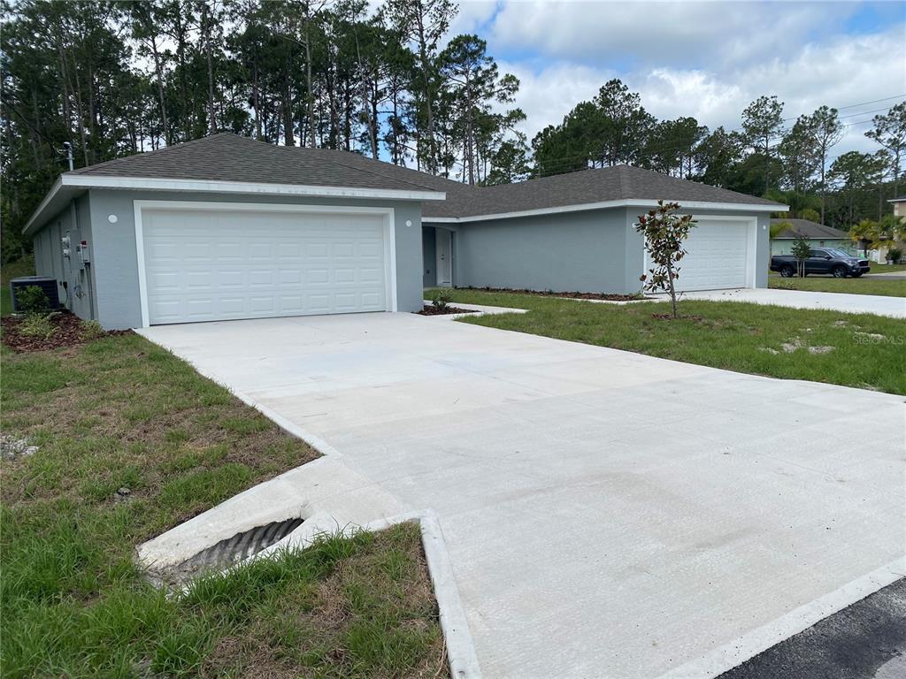 A light gray duplex with two garage doors and a concrete driveway under a cloudy sky — 2 RYAPPLE LANE UNIT A, PALM COAST, FL