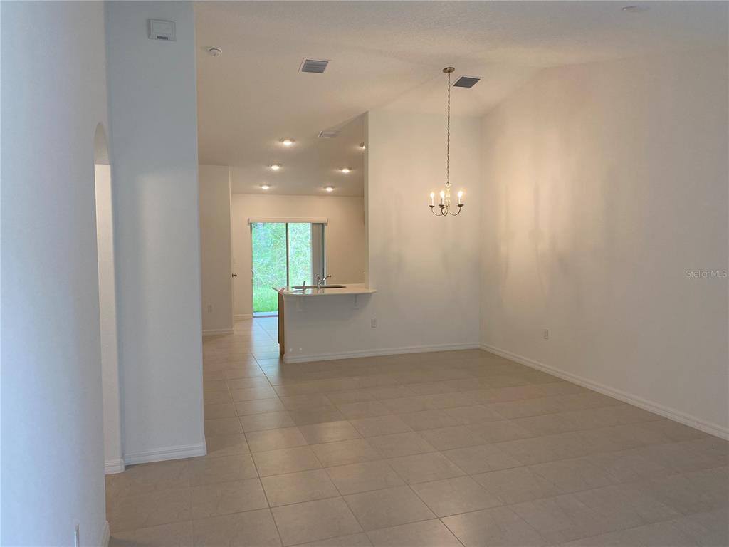 An open-concept dining area features tile flooring, a chandelier, and a view of the kitchen — 2 RYAPPLE LANE UNIT A, PALM COAST, FL