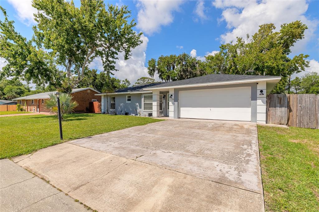 A single-story house with a white garage door, gray siding, and a concrete driveway — 2616 WOODLAND DRIVE, EDGEWATER, FL