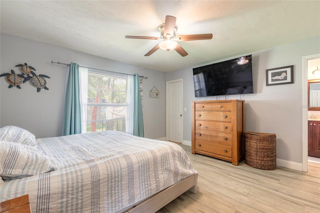 A bedroom features a bed, a wooden dresser with a television, and light wood flooring — 2616 WOODLAND DRIVE, EDGEWATER, FL