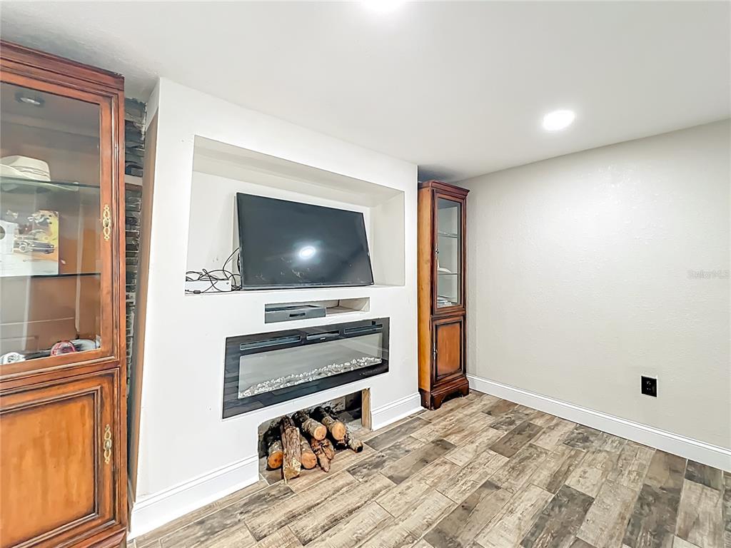A room features a wall-mounted television above an electric fireplace with logs and wood flooring — 638 NW 6TH TERRACE, OCALA, FL