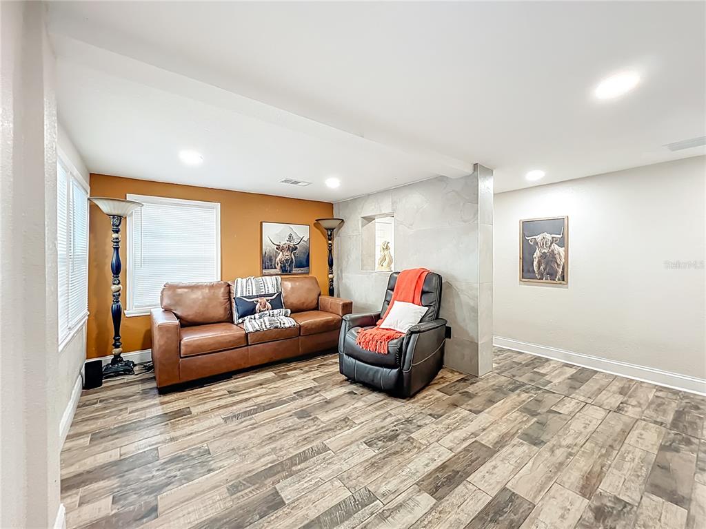 A living room features a brown leather sofa, a black recliner, and wood-look tile flooring — 638 NW 6TH TERRACE, OCALA, FL
