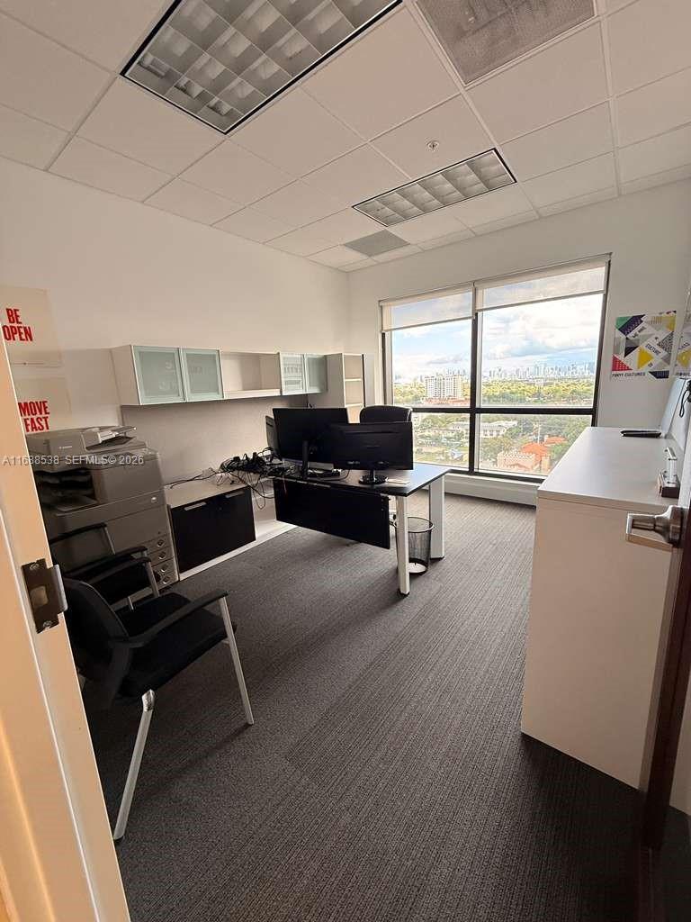 An office with a desk, two monitors, a printer, and a large window with city views — 2020 Ponce De Leon Blvd, Coral Gables FL 33134, CORAL GABLES, FL