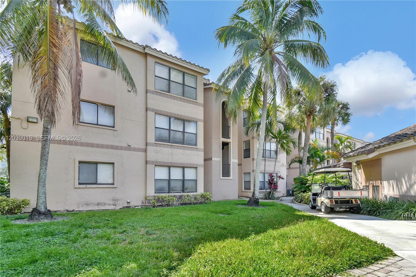 A three-story tan apartment building features palm trees, a grassy lawn, and a golf cart — 2866 S University Dr # 5105, Davie FL 33328, DAVIE, FL