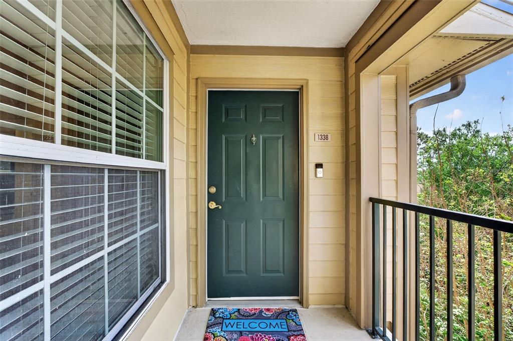 A dark green front door with a welcome mat sits on a covered apartment balcony — 7800 POINT MEADOWS DRIVE UNIT 1338, JACKSONVILLE, FL