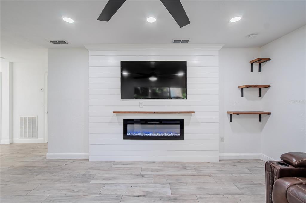 A living room features a white shiplap fireplace wall, a mounted television, and floating shelves — 640 ORANGE VALLEY CIRCLE, LAKELAND, FL