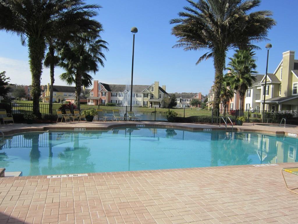 A concrete walkway leads between two multi-story apartment buildings toward a lake and trees — 9013 LEE VISTA BOULEVARD UNIT 1901, ORLANDO, FL