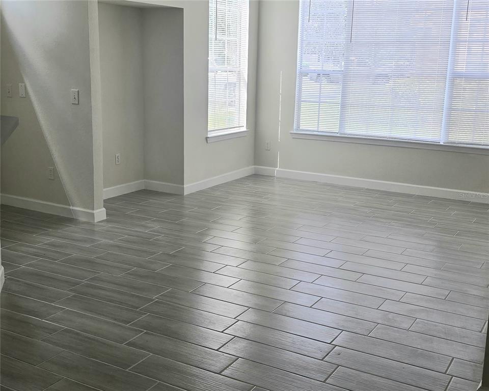 An empty room features gray wood-look tile flooring, light-colored walls, and large windows with blinds — 9013 LEE VISTA BOULEVARD UNIT 1901, ORLANDO, FL
