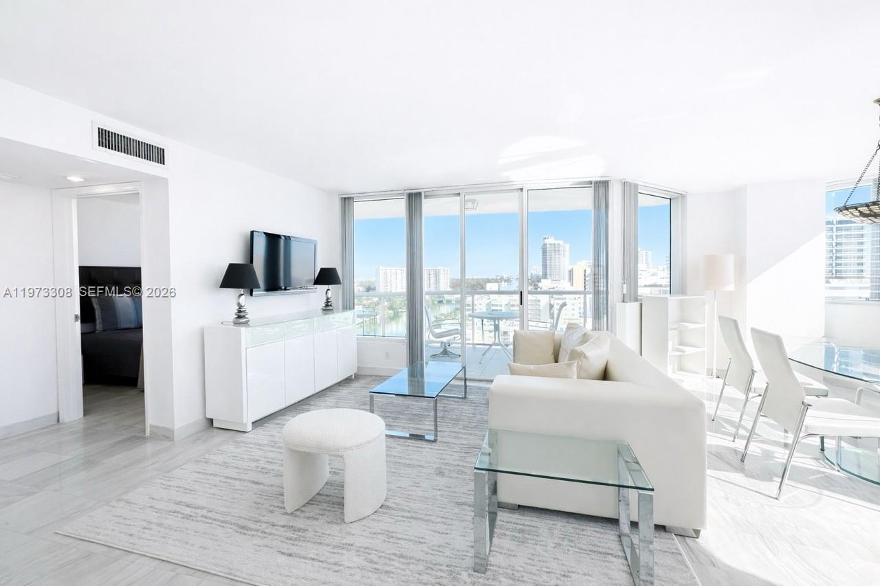 A bright living room features white furniture, a glass coffee table, and a balcony view — 3411 Indian Creek Dr, Miami Beach FL 33140, MIAMI BEACH, FL