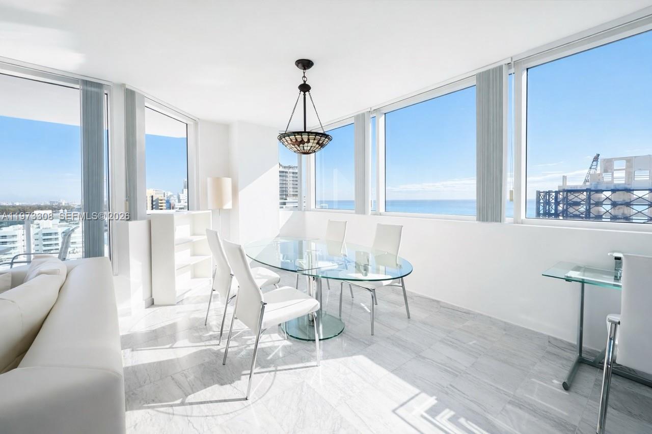 A dining area with a glass table, white chairs, marble floors, and floor-to-ceiling ocean views — 3411 Indian Creek Dr, Miami Beach FL 33140, MIAMI BEACH, FL