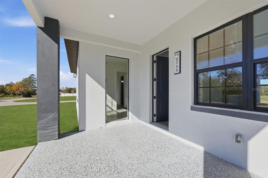 A covered porch features a speckled concrete floor, a dark front door, and a window — 17181 SW 20TH COURT ROAD, OCALA, FL