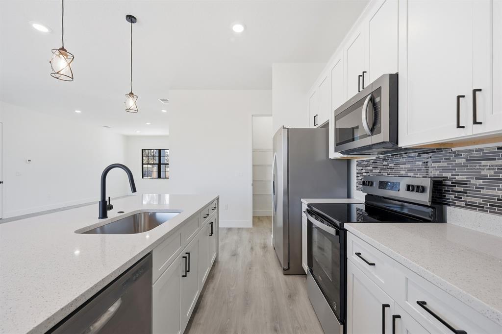 A bright, open-concept kitchen and living area featuring white cabinets, stainless appliances, and light flooring — 17181 SW 20TH COURT ROAD, OCALA, FL