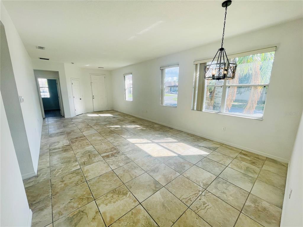 An empty room with tan tile flooring, a hanging light fixture, and several windows — 2728 PORTCHESTER COURT, KISSIMMEE, FL